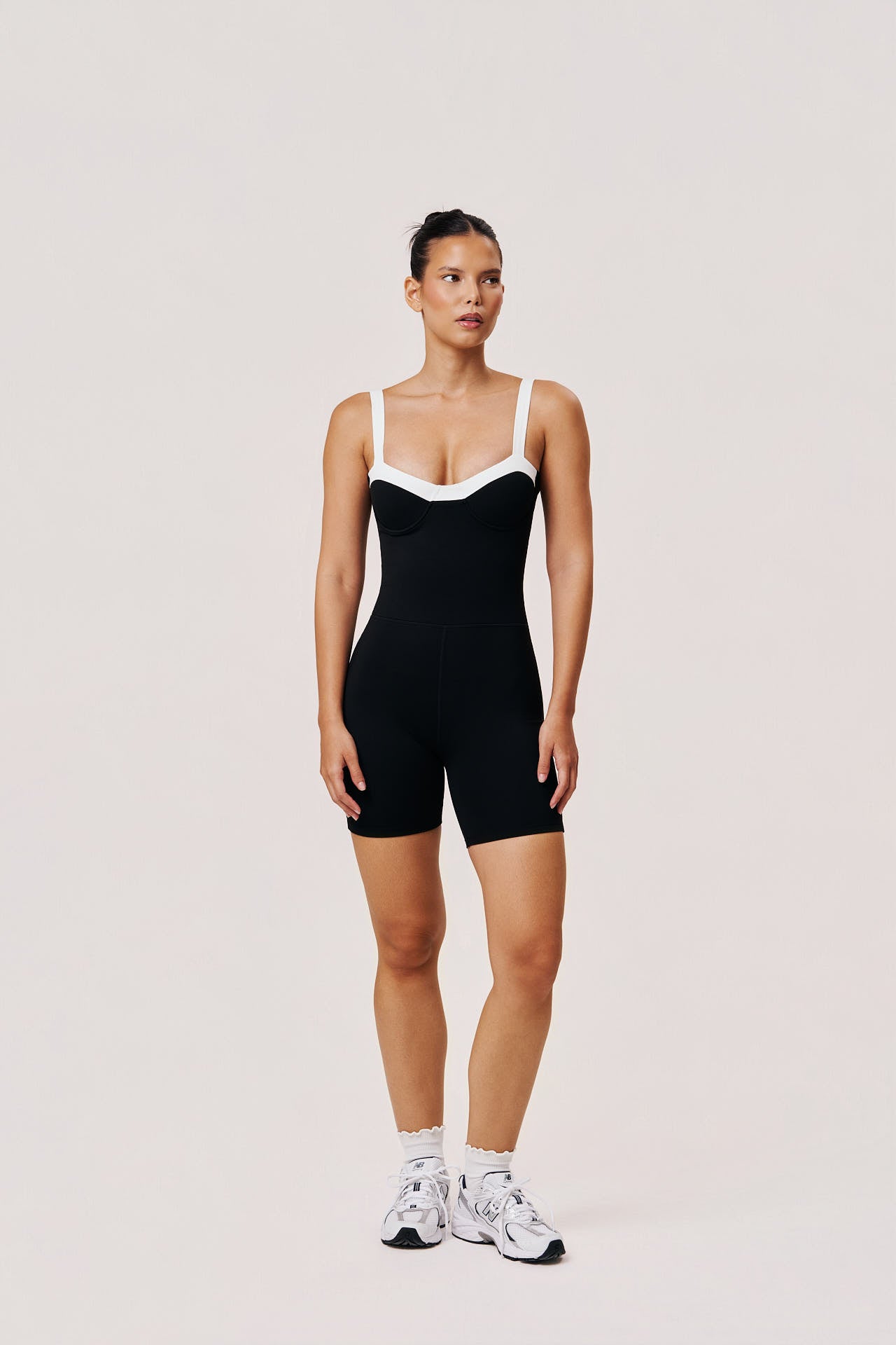 Woman wearing a black bodysuit with white trim on a plain background