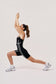 Woman in a black athletic outfit performing a stretching exercise on a light background